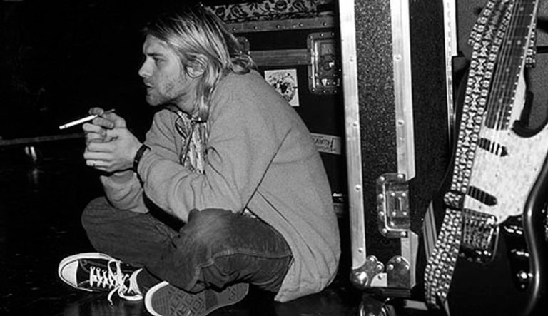 Kurt Cobain portant des Converse Chuck Taylor en coulisses Kurt Cobain assis en coulisses avec une cigarette, portant des Converse Chuck Taylor All Star noires.