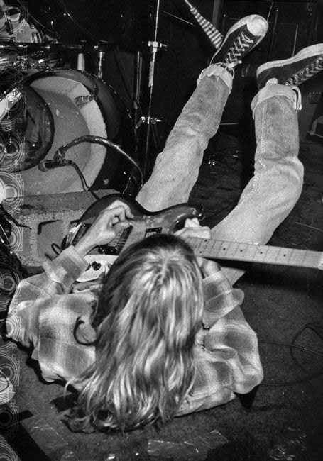 Kurt Cobain portant des Converse Chuck Taylor sur scène Kurt Cobain jouant de la guitare sur scène avec des Converse Chuck Taylor All Star noires et un jean délavé.