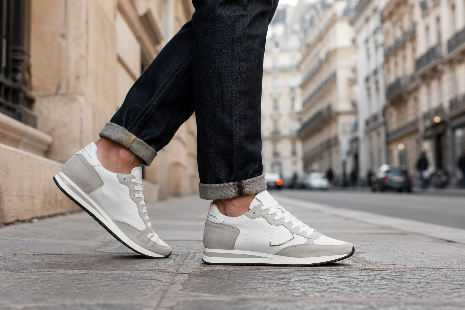 Philippe Model Tropez portée avec un jean homme Homme portant une paire de baskets Philippe Model Tropez blanches et grises avec un jean dans une rue urbaine.