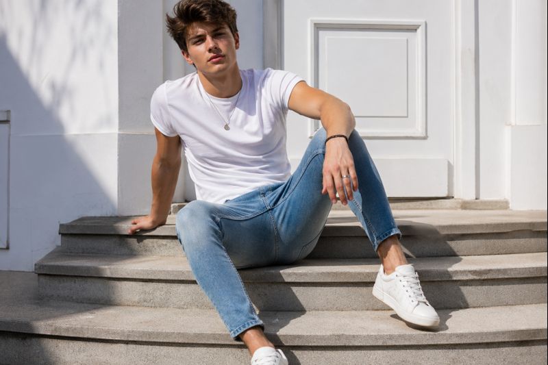 Homme au style twink portant un jean ajusté, un t-shirt blanc et des sneakers propres, illustrant un look jeune, simple et esthétique.