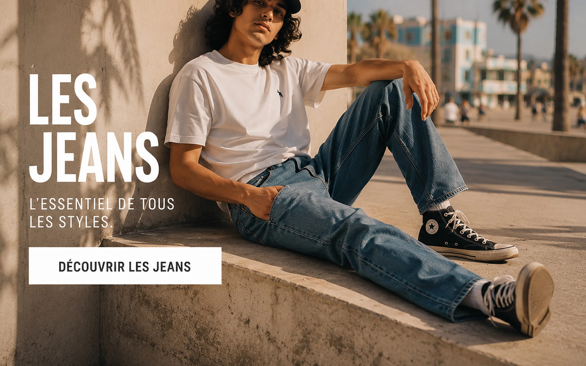 Jeans homme casual – Style urbain et moderne Jeune homme portant un jean bleu casual assis en extérieur dans une ambiance urbaine et ensoleillée