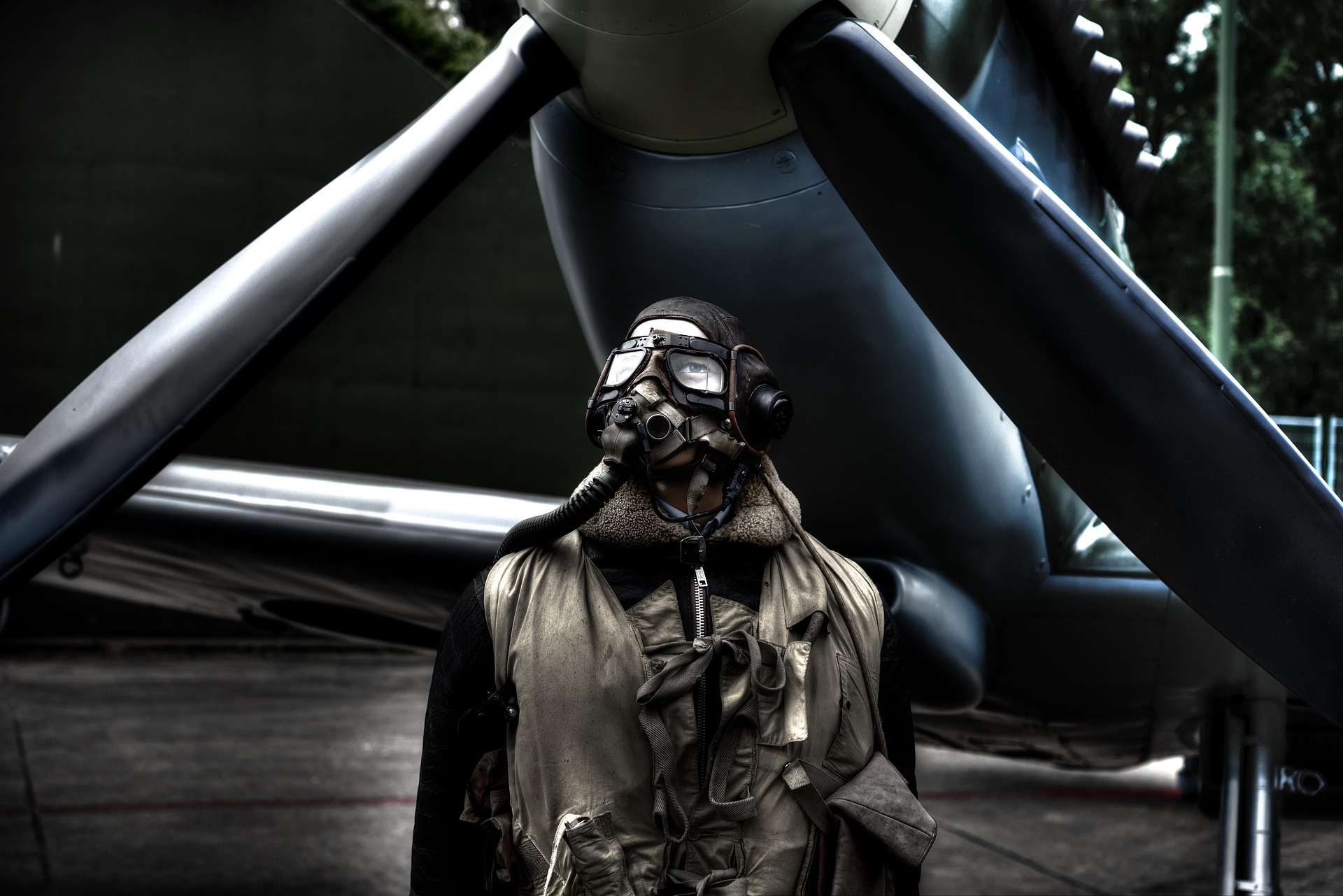 Pilote d'aviation vintage portant un équipement de vol en cuir devant l'hélice d'un avion ancien.